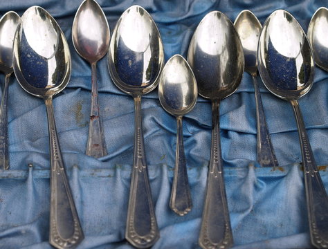 Group of aged dirty spoons lying on a dirty blue cloth (flea market)