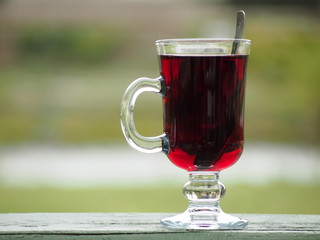 Hot red beverage in a glass cup lying outdoor on a green wooden board.