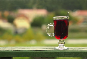Hot red beverage in a glass cup lying outdoor on a green wooden board.