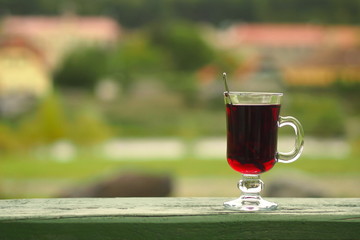 Hot red beverage in a glass cup lying outdoor on a green wooden board.