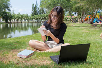 young woman working on laptop outdoors. image of female student working on laptop while sitting in a park with books