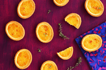 Mini lemon tarts with thyme on deep lilac background, top view