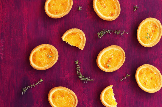 Tartlets with lemon filling and thyme on deep lilac background, top view