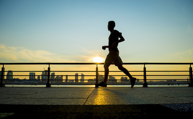 Obrazy na Plexi  Sylwetka biegacza biegnącego o zachodzie słońca przed panoramą miasta city