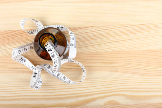 diet pills with measuring tape on wooden background
