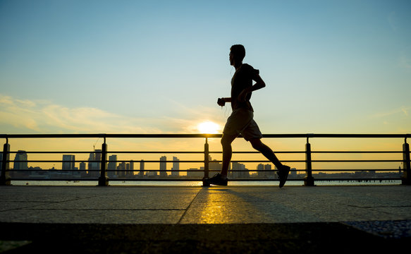 Silhouette of jogger running at sunset in front of the city skyline 