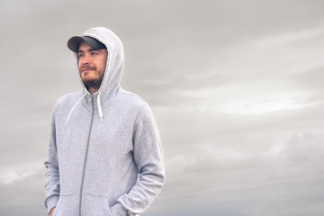 Young man wearing a hoodie and a baseball cap with a cloudy day
