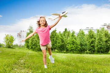 Happy girl holds airplane toy with one leg up