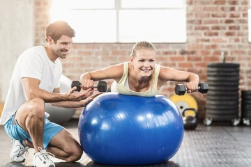 Obraz premium Male trainer helping young woman with the dumbbells 