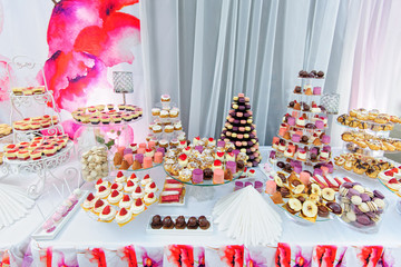 Wedding decoration with colorful cupcakes, eclairs, souffle, meringues, muffins, macarons and cookies. Elegant and luxurious event arrangement with sweets. Wedding dessert table in pink colors