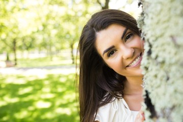 Portrait of smiling woman behind tree trunk