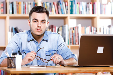 Fototapeta premium Serious young man sitting at the table with laptop