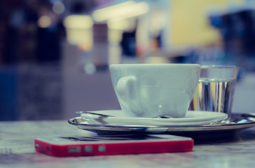 A cup of coffee on a tray and a smart phone on a table