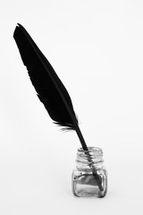 black feather and ink pot above on white paper - studio shot