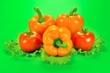 Three sweet pepper and two tomatoes with a lettuce leaf on a green background