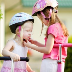 Little girl helping her sister to put a helmet on