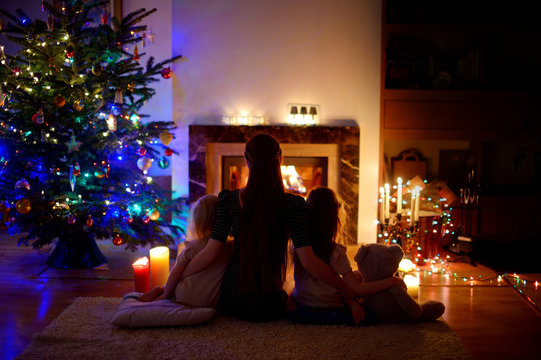 Young mother and daughters sitting by a fireplace on Christmas