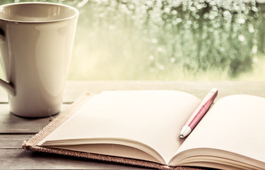 Pen on open notebook and coffee cup in rainy day