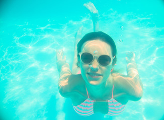 Young girl in sunglasses swimming underwater