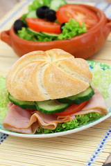 Lunch consisting of ham roll with lettuce, tomato and cucumber and green side salad
