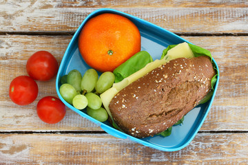 Healthy school lunch box containing brown cheese roll, mandarine, grapes and cherry tomatoes on...