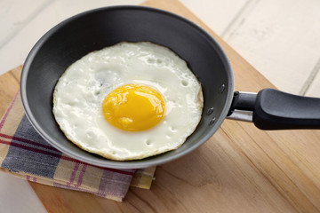 Fried egg in pan. Fried egg inside pan over cutting board in domestic kitchen.