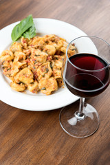 Wine and Italian pasta with basil on white plate on wooden table with shallow depth of field.
