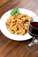 Wine and Italian pasta with basil on white plate on wooden table with shallow depth of field.