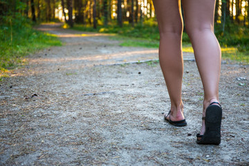 female legs in sandals walking on forest road