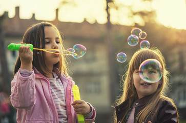 Young girls having a good time in park, blowing bubbles and smiling. Selective focus on girl on right. Old film look.