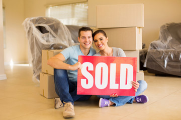 couple holding sold sign surrounded by cardboard boxes