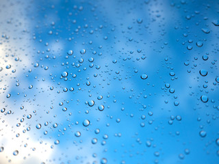 Raindrops on the glass with blurry blue sky and white cloud.