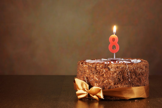 Birthday chocolate cake with burning candle as a number eight on brown background