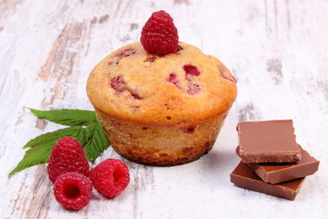 Fresh baked muffins with raspberries and chocolate on wooden background, delicious dessert