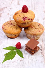 Fresh baked muffins with raspberries and chocolate on wooden background, delicious dessert