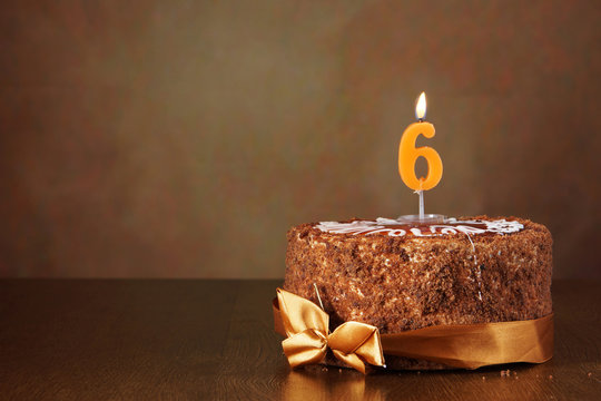 Birthday chocolate cake with burning candle as a number six on brown background