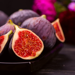 Ripe delicious figs and autumn flowers on black wooden background. Selective focus. Toned square...