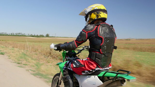 Enduro racer in motorcycle protective gear riding bike side rear view vehicle shot