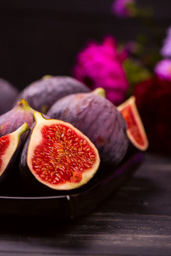 Ripe delicious figs and autumn flowers on black wooden background. Selective focus. Toned image