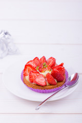 cake with strawberries and custard on a white plate with a spoon. on a light wooden background. top view. Portion pastries