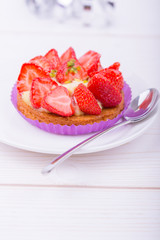 cake with strawberries and custard on a white plate with a spoon. on a light wooden background. top view. Portion pastries