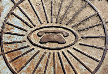 Telephone symbol icon on rusty manhole cover.