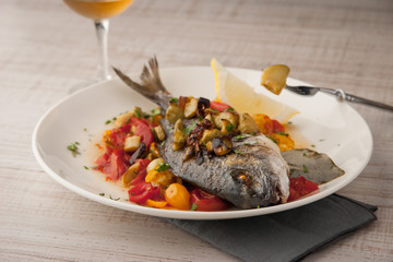 Fried dorado with vegetables  on the ceramic plate with glass of vine horizontal