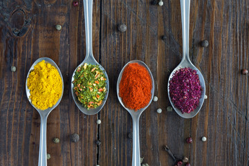 Variety of Eastern Spices in Silver Spoons Close up Image of Grey Metal Spoons with Selection of Aromatic Seasonings on Rough Dark Natural Wooden Board Table