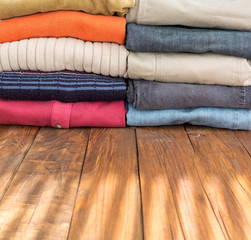 Obraz na płótnie Canvas Jeans Pants and Classic Wool Sweaters on Wood Many Colorful Clothing Neatly Stacked in Two Rows on Natural Wooden Board Desk Illuminated by Sunlight Stripes Throw Venetian Blinds