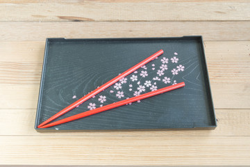 Red chopsticks on black tray Sakura's design wooden background