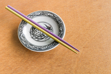 Purple and Yellow chopsticks on old dish wooden background