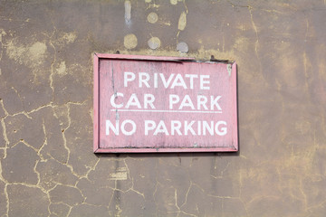 Faded and cracked wooden 'Private Car Park - No Parking' sign on wall