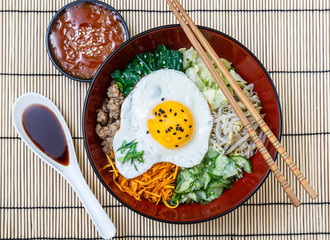 bibimbap in a bowl with sauces on bamboo mat, korean dish