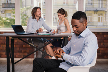 African american man sitting on the chair in business office and waiting for job interview looking at the clock
